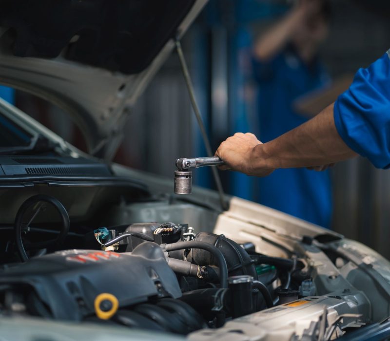 Asian mechanic repairing a car in auto repair shop.